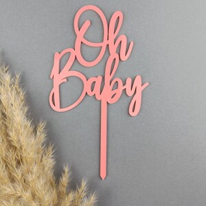 May include: Pink wooden cake topper with the words "Oh Baby" in a cursive font.