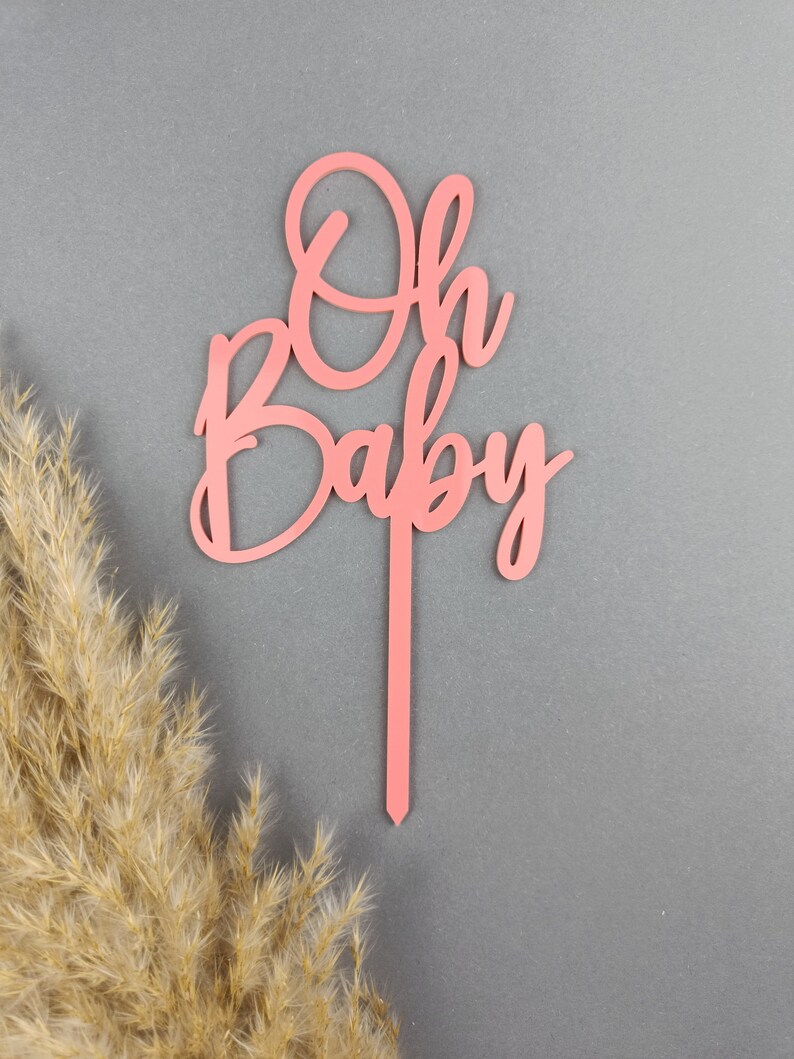 May include: Pink wooden cake topper with the words "Oh Baby" in a cursive font.