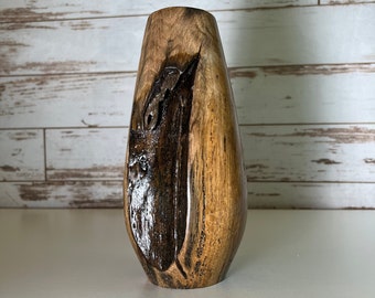 May include: A wooden vase with a dark brown and light brown wood grain pattern. The vase is shaped like a teardrop and has a smooth, polished finish.