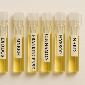 May include: Six small glass vials with white labels and clear caps, each containing a golden-yellow liquid. The labels read "EXODUS", "MYRRH", "FRANKINCENSE", "CINNAMON", "HYSSOP", and "NARD".