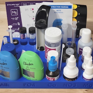 May include: A blue plastic test kit for measuring water parameters in a marine aquarium. The kit includes test tubes, reagents, and a colorimeter. The test kit is labeled with the following parameters: Alkalinity, Phosphate, Calcium, Nitrate, and Magnesium.