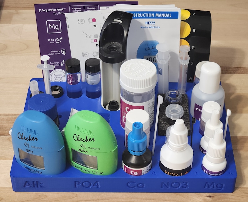 May include: A blue plastic test kit for measuring water parameters in a marine aquarium. The kit includes test tubes, reagents, and a colorimeter. The test kit is labeled with the following parameters: Alkalinity, Phosphate, Calcium, Nitrate, and Magnesium.