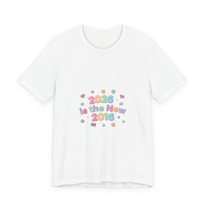 Puede incluir: Camiseta blanca con un gráfico colorido que dice "2026 is the New 2016". El diseño incluye corazones, estrellas y caras sonrientes en colores pastel. Una camiseta casual y divertida.
