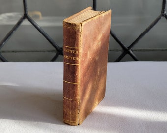 May include: A vintage, small, brown book titled "Letter Writer" with gold lettering. The book has a worn, textured cover and aged, yellowed pages. The spine is a darker brown, and the book appears to be well-loved and used.