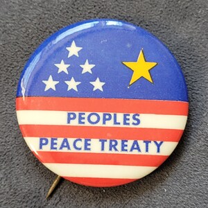 May include: A red, white and blue button with a yellow star and the text "PEOPLES PEACE TREATY".