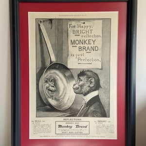 Könnte beinhalten: Eine Vintage-Werbung für Monkey Brand Seife. Die Anzeige zeigt einen Affen, der in eine glänzende Metallpfanne schaut, die ein mattes Bild des Affen reflektiert. Der Text lautet "Für glückliche, helle Reflexionen, Monkey Brand ist einfach Perfektion." und "Reflexionen. Brooke's Seife Monkey Brand Wäscht keine Kleidung."