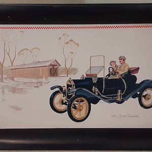 Puede incluir: Una bandeja de metal negro con fondo blanco que presenta un coche antiguo con dos personas dentro. El coche está pasando por un puente de madera y árboles. El texto "1917 Ford Touring" está impreso debajo del coche.