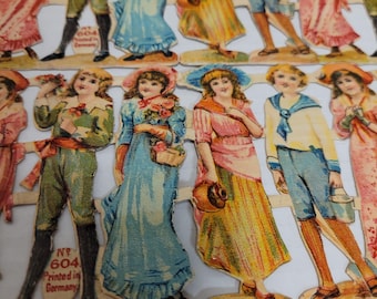 May include: A vintage set of paper dolls featuring a variety of characters, including a girl in a blue dress, a boy in a sailor suit, and a girl in a pink dress. The dolls are printed in Germany and are in good condition.