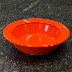 Puede incluir: Un cuenco de cerámica naranja vibrante con un diseño ancho y poco profundo. El cuenco tiene un acabado liso y brillante y un borde ligeramente elevado. El interior es de color naranja brillante, perfecto para servir alimentos.