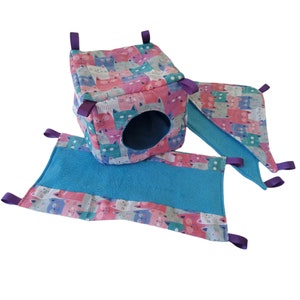 May include: A pink and blue cat-themed hanging hammock for small pets. The hammock has a cube-shaped sleeping area with a round entrance and two hanging platforms.