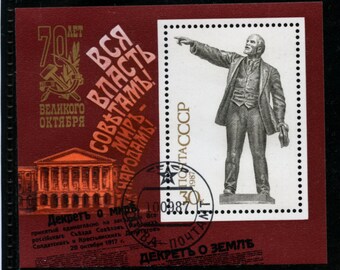 Könnte beinhalten: Eine Briefmarke zum 70. Jahrestag der Großen Oktoberrevolution. Die Briefmarke zeigt eine Person, die mit dem Finger zeigt, ein Gebäude und Text auf Russisch. Die Briefmarke ist rot und weiß.