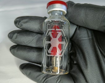 Könnte beinhalten: Ein klares Glasfläschchen mit einem roten Gummistopfen und einem roten Symbol im Inneren. Das Symbol ist ein stilisierter Stern mit sechs Zacken, umgeben von einem Sechseck. Das Fläschchen befindet sich in einer behandschuhten Hand.