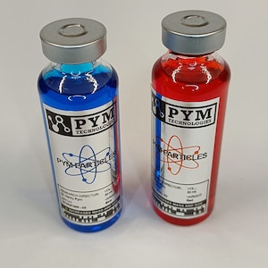 Puede incluir: Dos viales de vidrio con tapas plateadas, uno lleno de líquido azul y el otro de rojo. Cada vial tiene una etiqueta con "PYM TECHNOLOGIES" y "PYM-PARTICLES" impreso. El vial azul está etiquetado "Azul" y el rojo "Rojo".