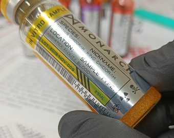 May include: A yellow vial labeled "MONARCH" with black text and a skull and crossbones symbol. The label reads "Species: Titanus Ghidorah, Nickname: King Ghidorah, Sample Type: Antarctica Facility Blood, Lot: 2019-NOV 009".