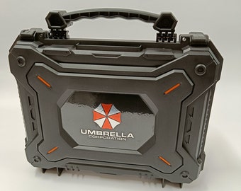 Könnte beinhalten: Schwarzer Kunststoffkoffer mit Griff und einem roten und weißen Schirmlogo mit der Aufschrift "Umbrella Corporation".