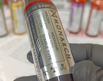 May include: A silver vial labeled "MONARCH" with a biohazard symbol and a skull and crossbones. The label also includes the text "VITRO SAMPLE", "SPECIES: TITANUS KONG KING KONG", "NICKNAME: KING KONG", "LOCATION: HOLLOW EARTH BLOOD", "SAMPLE TYPE: BLOOD", and "LOT: 1988-SEP 018". The vial contains a dark red liquid.