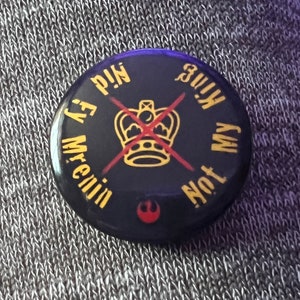 Pode incluir: Um bot&atilde;o preto com um X vermelho sobre uma coroa dourada e o texto "Not My King" e "Mr. Evil's P.I.N." ao redor da coroa.