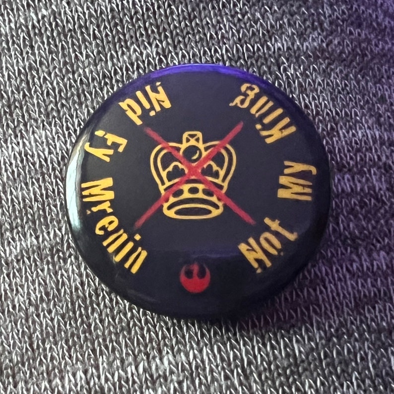 Pode incluir: Um bot&atilde;o preto com um X vermelho sobre uma coroa dourada e o texto "Not My King" e "Mr. Evil's P.I.N." ao redor da coroa.