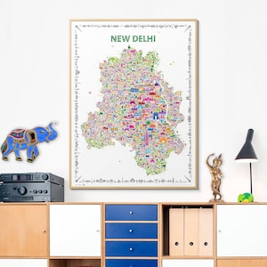 A vibrant, illustrated map of New Delhi, India, features numerous colorful landmarks and buildings. The map is framed and displayed on a wall above a light wood cabinet with blue drawers.  A small, blue, decorative elephant and a gold statue are also visible. The map's title, 'NEW DELHI,' is prominently displayed at the top. The overall aesthetic is modern and eclectic, blending cultural elements with contemporary design.