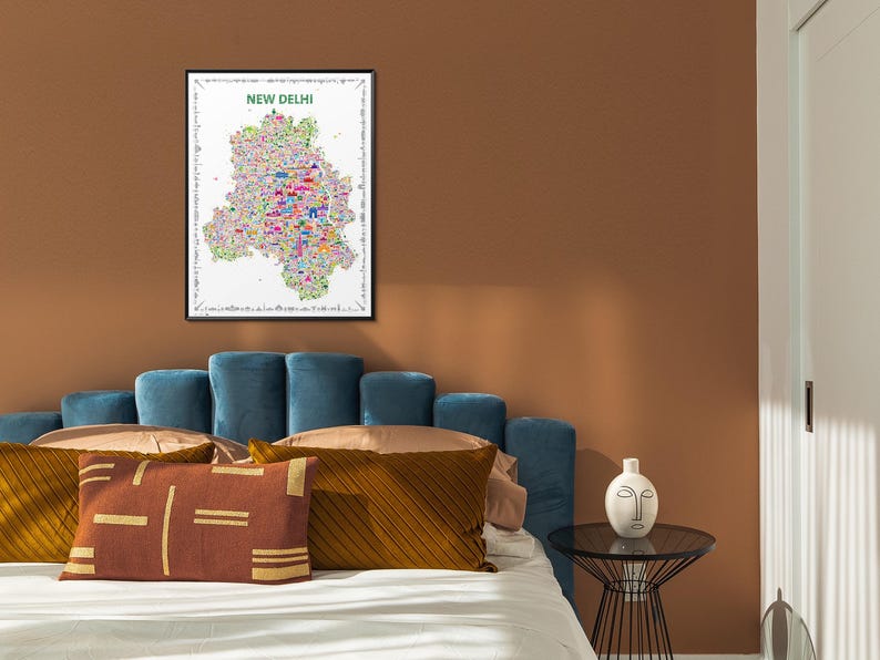 A framed wall art print featuring a colorful, detailed map of New Delhi, India. The map is filled with various small, vibrant icon illustrations of landmarks and cultural icons, set against a white background with a black frame. It is an artistic artwork.