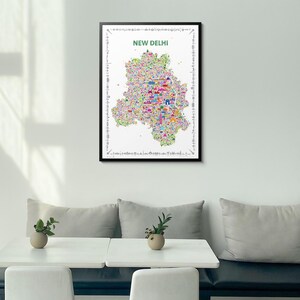A framed wall art print featuring a colorful, detailed map poster of New Delhi. The map is filled with small, vibrant illustrations of landmarks and city elements, set against a white background with the text NEW DELHI at the top.