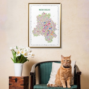 A framed wall art print featuring a colorful, detailed map poster of New Delhi, India. The map is set against a white background with the text NEW DELHI printed in green at the top, surrounded by a decorative border of small black icons.