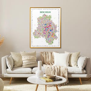 A rectangular wall art print featuring a colorful, detailed illustrated map of New Delhi. The map poster is set against a white background with the text NEW DELHI printed in green at the top, surrounded by a decorative border of small icons. It is a wall art travel souvenir artwork.