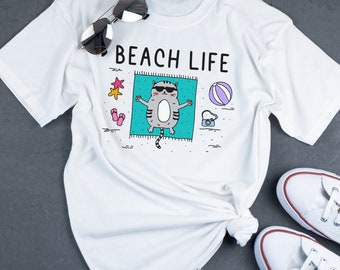 May include: White t-shirt with a cartoon cat wearing sunglasses and lying on a beach towel. The text "BEACH LIFE" is printed on the shirt.