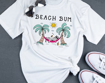 May include: White t-shirt with a graphic of a cat relaxing in a hammock between two palm trees. The text "Beach Bum" is printed above the graphic.