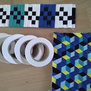 Könnte beinhalten: Nahaufnahme von sechs Rollen weißen Klebebands, einem Stoffstreifen mit schwarz-weißem Karomuster und einem Stoffstreifen mit blauem, grünem und gelbem geometrischem Muster.