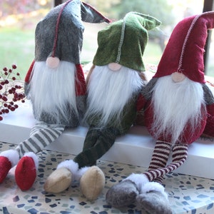 May include: Three gnomes with long legs and white beards sitting on a white box. The gnomes are wearing red, green, and gray hats and striped pants.