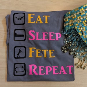 May include: Gray t-shirt with a checklist design that says "Eat, Sleep, Fete, Repeat". The checklist items are illustrated with icons for a fork and knife, a bed, a dancing figure, and a curved arrow.