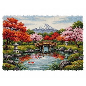 May include: A detailed needlepoint of a Japanese garden scene. The image features a pond with koi fish, a wooden bridge, and a snow-capped mountain in the background. Trees with red and pink foliage frame the scene, with stone lanterns on either side.