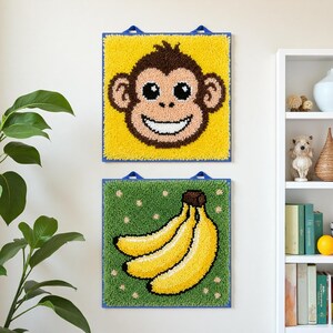 May include: Two square wall hangings with a monkey face and bananas. The monkey face is brown, tan, and black on a yellow background. The bananas are yellow with a brown stem on a green background.