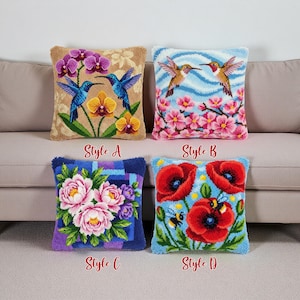 Op de afbeelding: Vier decoratieve sierkussens met geborduurde ontwerpen. Stijl A toont kolibries en orchideeën. Stijl B toont kolibries en roze bloemen. Stijl C toont roze en paarse bloemen. Stijl D heeft rode klaprozen en bijen.