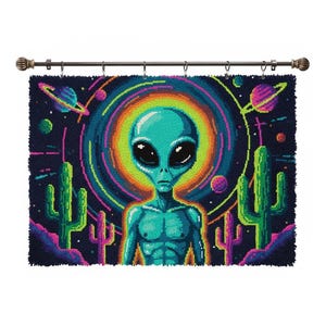 May include: A teal alien with large black eyes is centered on a dark blue tapestry. The alien is surrounded by a colorful, pixelated background of planets, cacti, and a rainbow-colored halo. The tapestry is hung on a decorative rod.