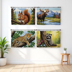May include: Four framed tapestry wall hangings featuring wildlife scenes. The images include a squirrel on a tree branch, a moose in a landscape, a jaguar on a tree branch, and a raccoon near a tree. Each tapestry is rectangular and mounted on a wooden rod.