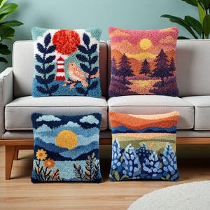Può includere: Quattro cuscini quadrati con ricamo a punch needle testurizzato. I disegni includono un faro con un uccello, un tramonto su una foresta, un sole su un paesaggio floreale e una catena montuosa con fiori blu, realizzati con filati colorati.