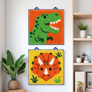 Può includere: Due decorazioni murali quadrate a tema dinosauri. Quella superiore presenta un T-Rex verde su sfondo arancione. Quella inferiore mostra un Triceratopo arancione su sfondo giallo. Entrambe hanno bordi blu e anelli per appenderle.