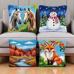 May include: Four decorative throw pillows with colorful designs. One features two horses, another a snowman in a winter scene, a third a landscape with a bridge, and the last a fox. The pillows are on a gray sofa.