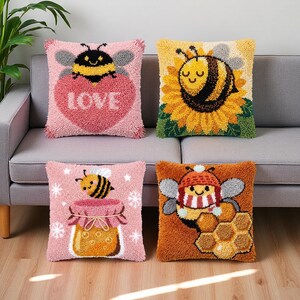 May include: Four decorative throw pillows with bee-themed designs. One pillow features a bee over a pink heart with the word "LOVE". Another shows a bee on a sunflower. The other two pillows have a bee over a jar of honey and a bee with a hat and scarf over a honeycomb.