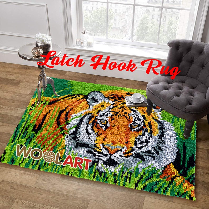 Puede incluir: Una alfombra de gancho de cierre que presenta la cara de un tigre con pelaje naranja, negro y blanco. El tigre est&aacute; rodeado de hierba verde. La alfombra est&aacute; etiquetada como "Latch Hook Rug" y "WOOLART".
