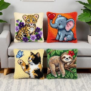Peut inclure: Quatre coussins décoratifs avec des motifs d'animaux. L'un représente un bébé léopard avec des fleurs violettes, un autre un éléphant tenant un cœur, un chat avec un papillon et un paresseux avec une fleur rouge. Les coussins sont sur un canapé gris.