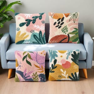 May include: Four square throw pillows with colorful abstract floral designs. The pillows feature a variety of colors, including pink, green, yellow, and blue. The pillows are arranged on a light blue sofa with wooden legs.