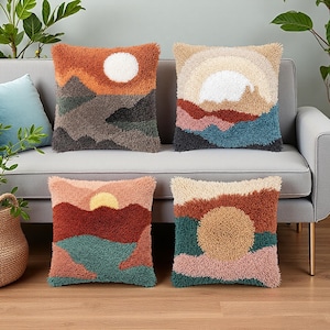 May include: Four square throw pillows featuring textured punch needle embroidery. Each pillow displays a unique landscape design with a sun or moon motif in shades of orange, beige, teal, brown, and pink, creating a layered, multi-colored scene.