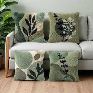 Op de afbeelding: Vier vierkante kussens met botanische ontwerpen. De kussens hebben verschillende groentinten, met zwarte en beige accenten. Elk kussen heeft een ander blad- of plantenpatroon, waardoor een samenhangende set voor woondecoratie ontstaat.
