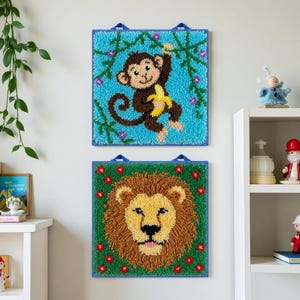 May include: Two square, textured wall hangings. The top one features a brown monkey holding a yellow banana against a blue background. The bottom one depicts a lion's face with a brown mane and yellow face on a green background.