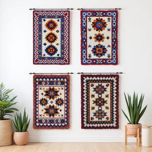 Könnte beinhalten: Vier rechteckige Wandbehänge mit aufwendigen geometrischen Mustern in Rot, Blau, Gelb und Weiß. Jedes Stück hat einen Fransenrand und ist an einer schwarzen Stange befestigt. Die Designs zeigen Stern- und Rautenmotive und schaffen eine lebendige, dekorative Darstellung.