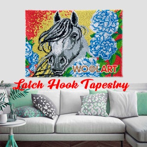 Puede incluir: Un tapiz de gancho de enganche que presenta un caballo blanco con una crin y cola negras, rodeado de flores azules y amarillas. El tapiz est&aacute; enmarcado con un borde rojo, amarillo y verde. El texto "WOOLART" es visible en la esquina inferior derecha.