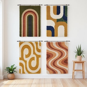 May include: Four rectangular wall hangings with abstract designs in various colors. The top left features a green background with a rainbow arch. The others have geometric patterns in mustard, white, and brown tones. They are mounted on a white wall.